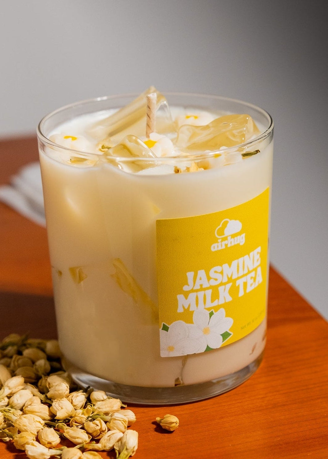 Glass of jasmine milk tea candle with a label on a wooden surface