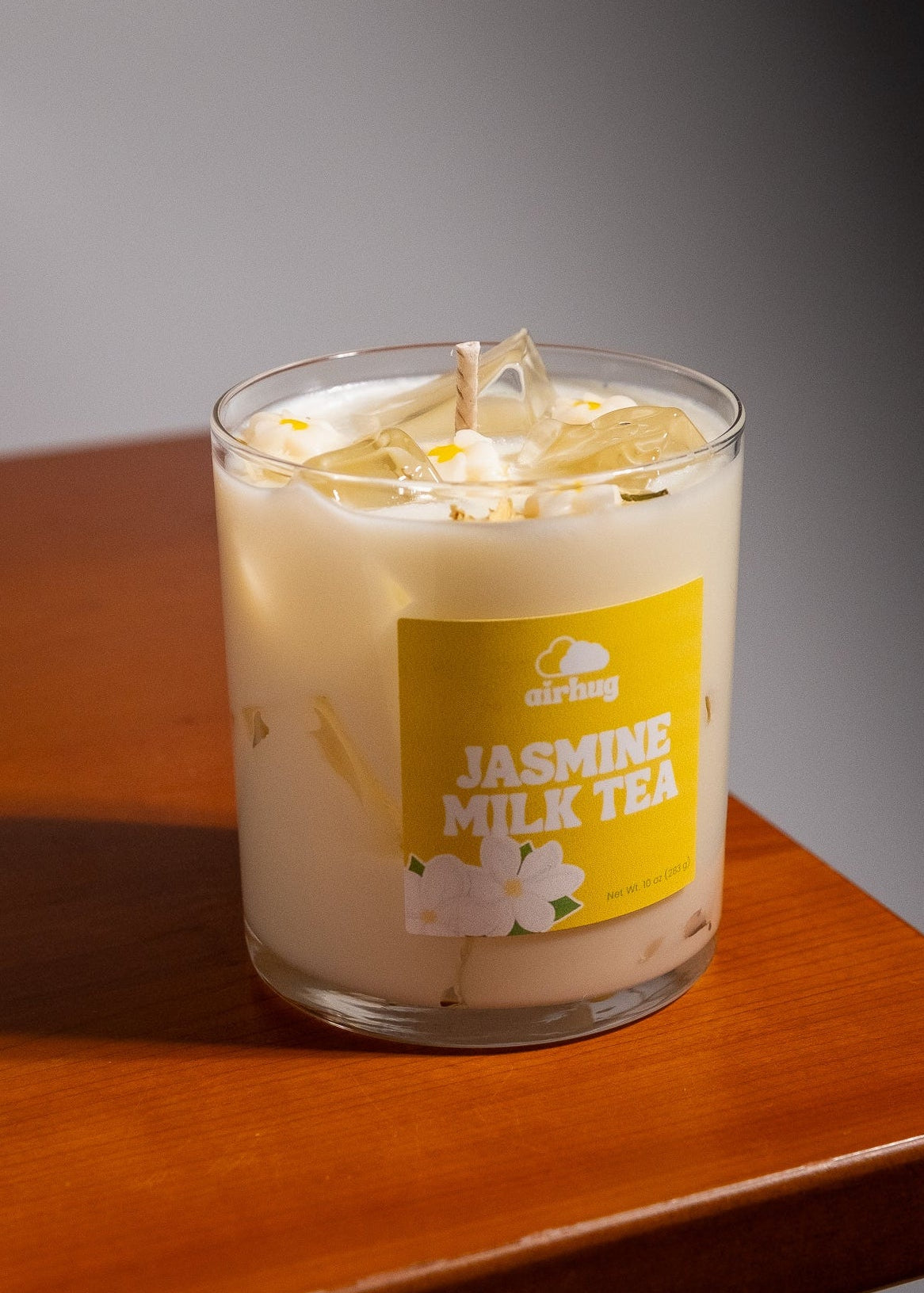Candle labeled 'Jasmine Milk Tea' with a yellow label on a wooden surface.