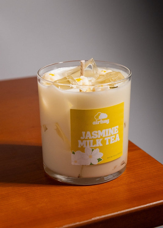 Candle labeled 'Jasmine Milk Tea' with a yellow label on a wooden surface.