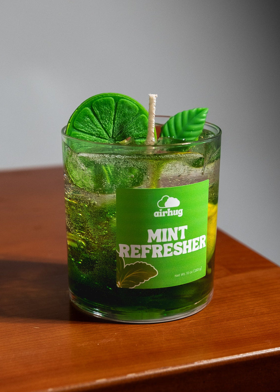 Green 'Mint Refresher' candle with lime slices and leaves on a wooden surface.
