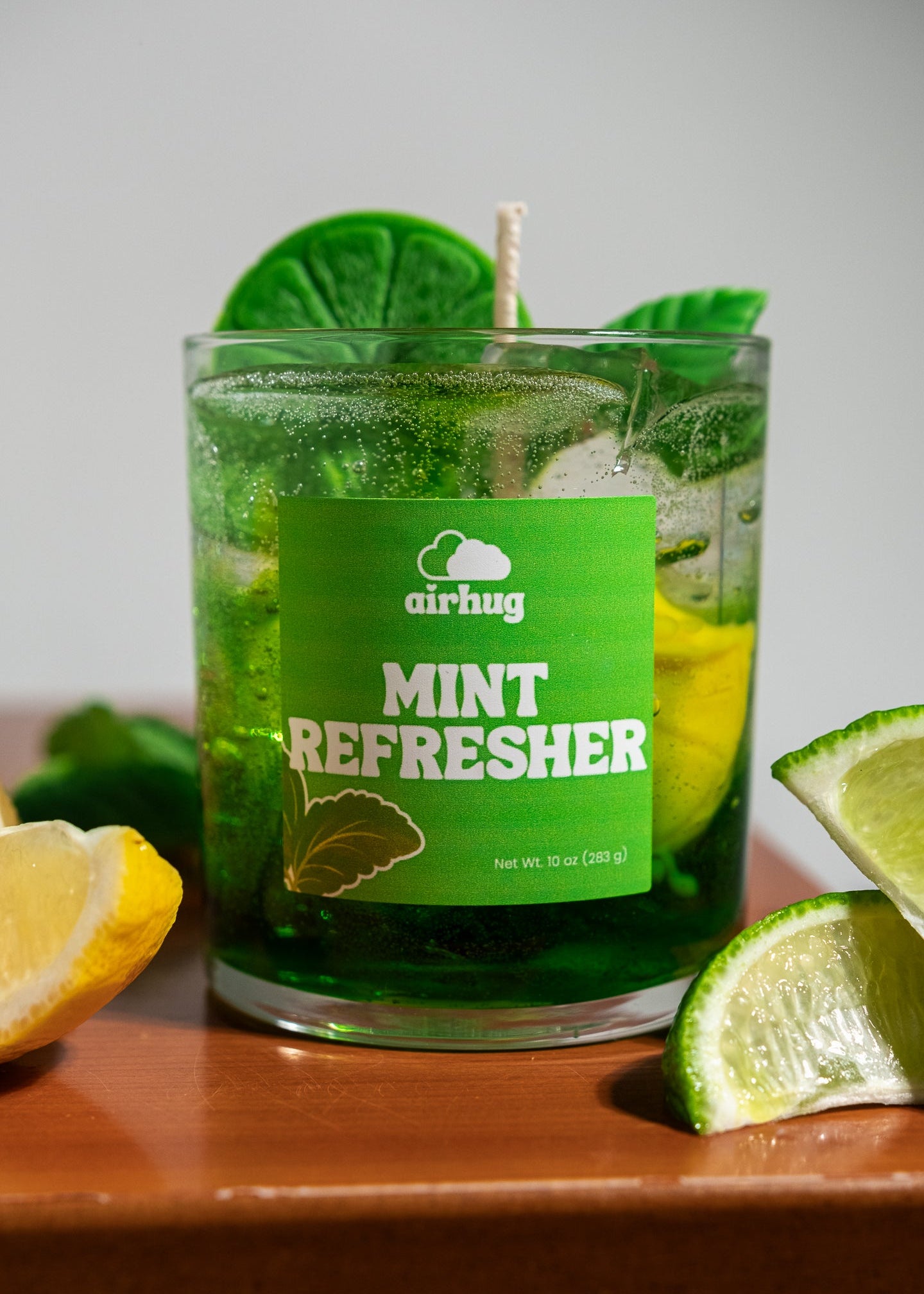 Green 'mint refresher' candle with lemon and lime slices on a wooden surface