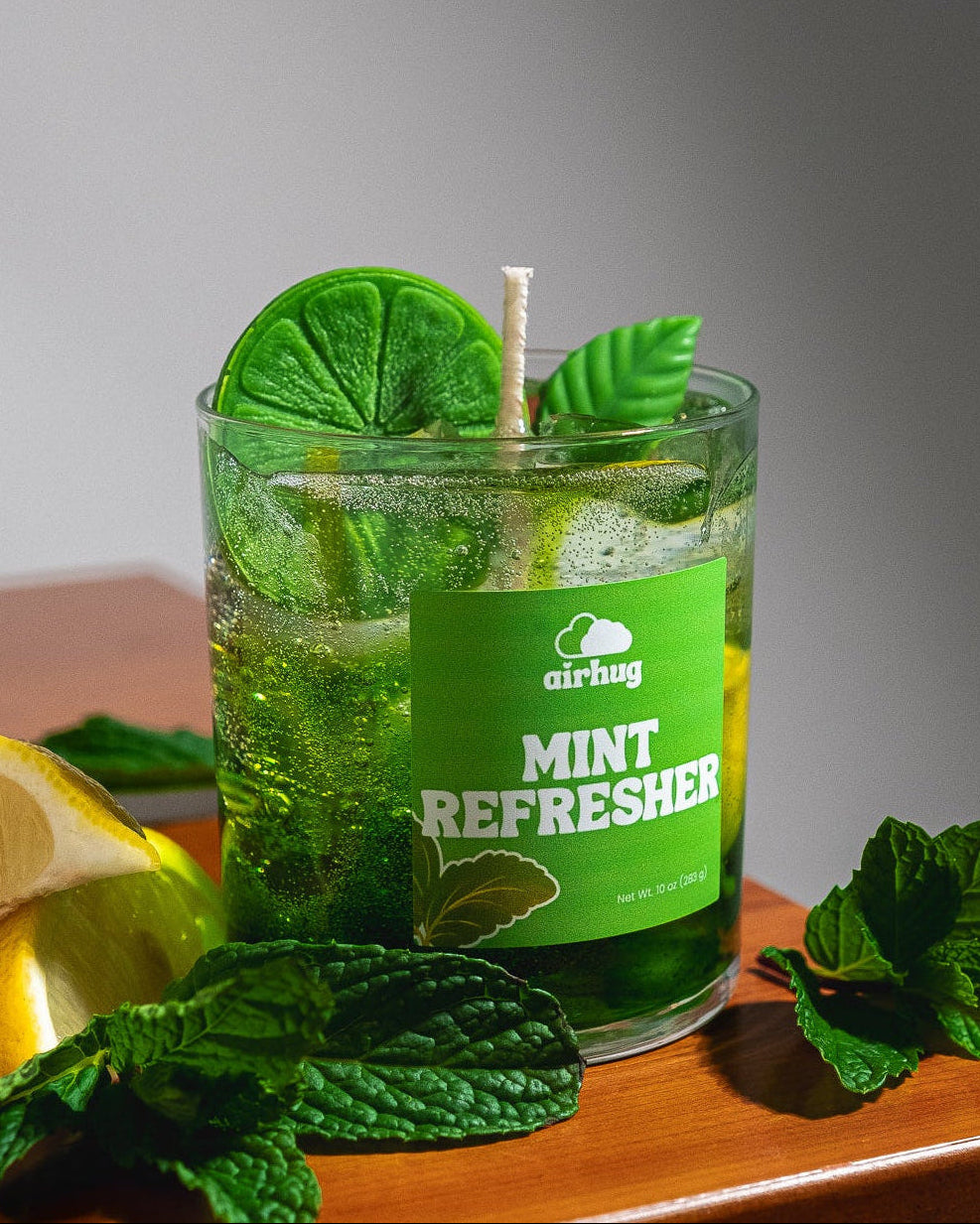 Glass container with a mint refresher candle, surrounded by mint leaves on a wooden surface.