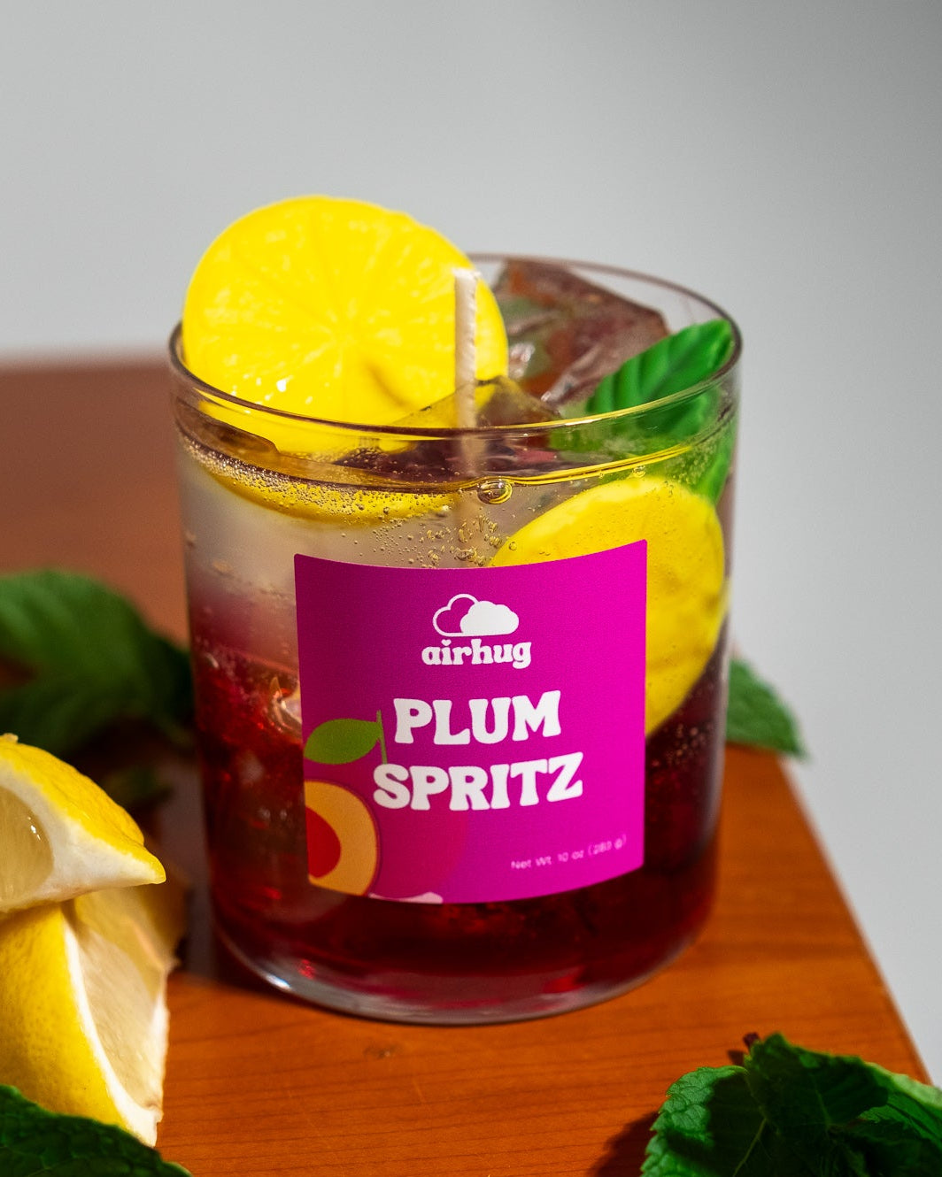 Glass of plum spritz candle with lemon slices and ice, featuring an 'airhug' label.