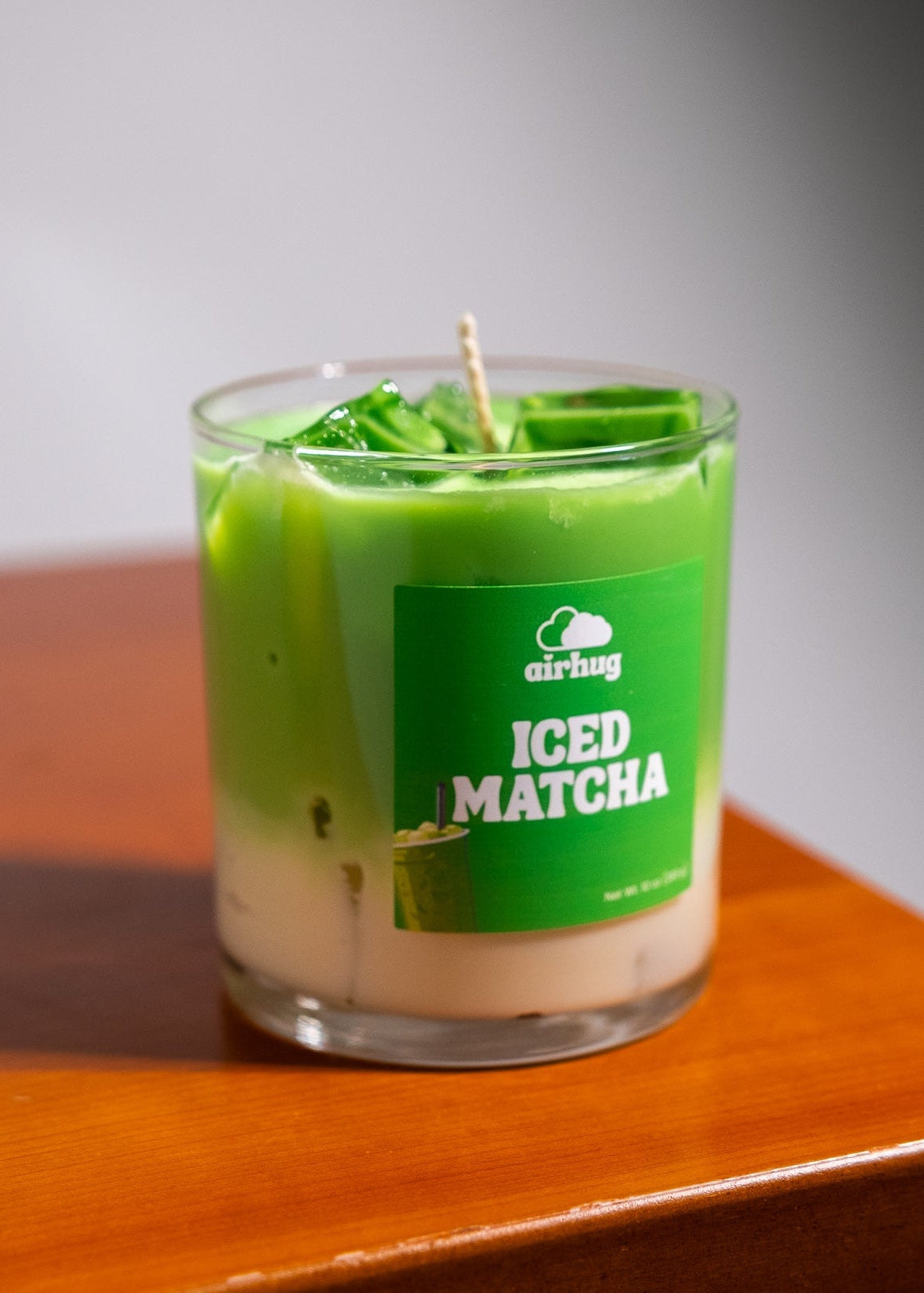 Green iced matcha candle in a glass container on a wooden surface
