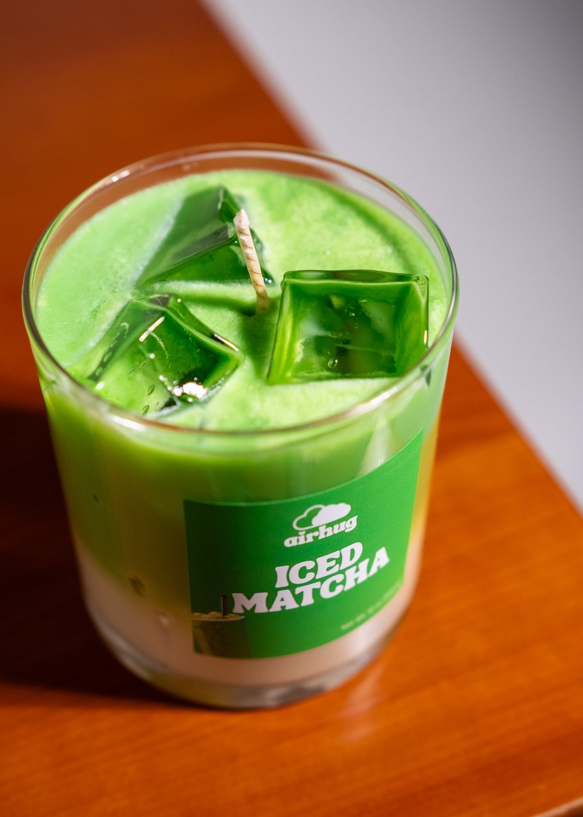Green iced matcha candle in a glass container on a wooden surface.