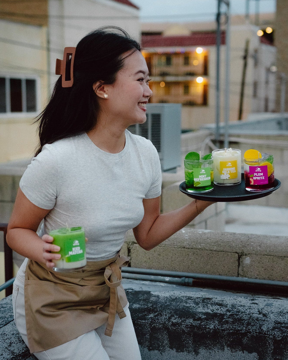Woman holding a tray with dessert candles that look like drinks on a rooftop setting