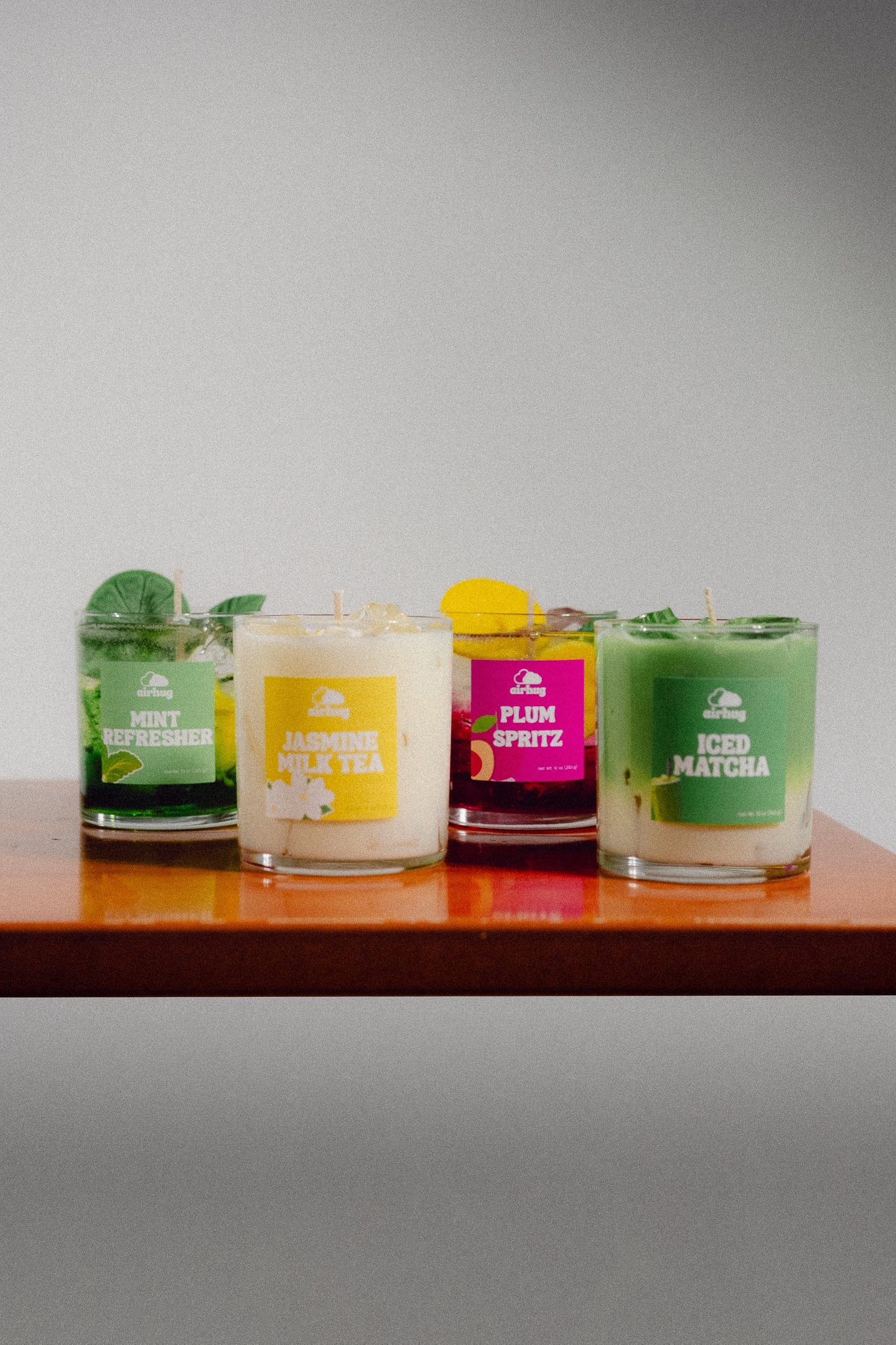 mint refresher, jasmine milk tea, plum spritz, and iced matcha dessert candles side by side on a wooden table.